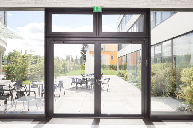 上置滑尺式闭门器 TS 5000 L-ISM, 安装在斯图加特 Häussler Global Office GmbH 公司中。 上置滑尺式闭门器系统合页异侧，用于双扇门，具有防恐慌功能和顺闭器。