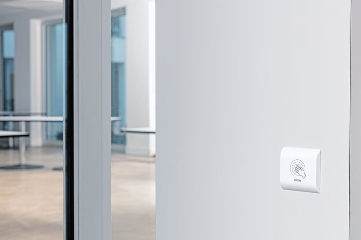 A non-contact proximity switch from GEZE mounted on a wall beside a glass sliding door in the Fux Campagna residential home.