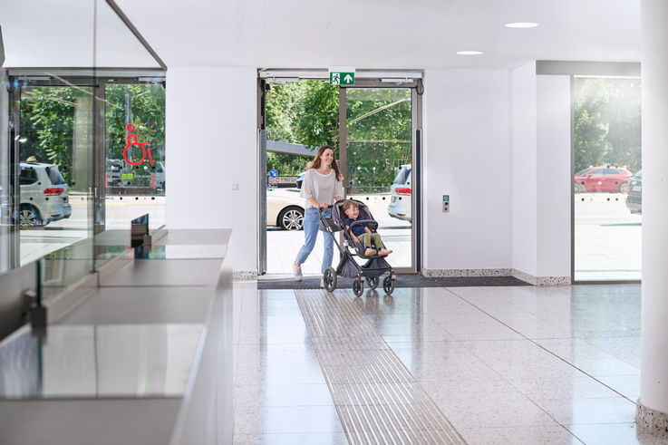 Woman with pram walks through automatic door into bright hospital corridor